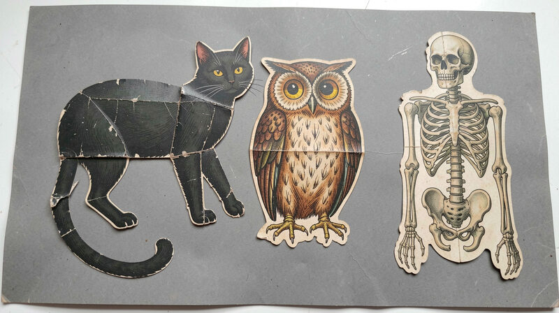 Flat paper Halloween die cuts of cats, owls and skeletons laid out between sheets of tissue on a museum work table.