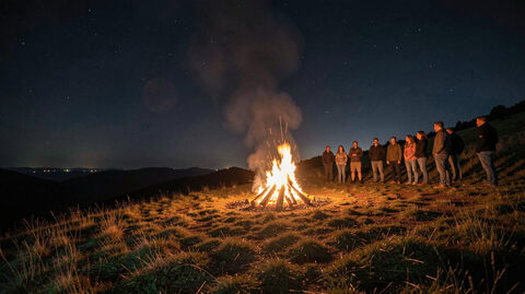 A small bonfire burning on a hillside at night with a group of people standing at a distance